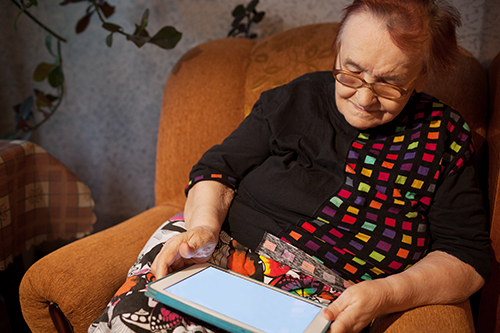 Elderly lady sitting in a comfortable arrnchair in her living room using a tablet computer as she surfs the internet