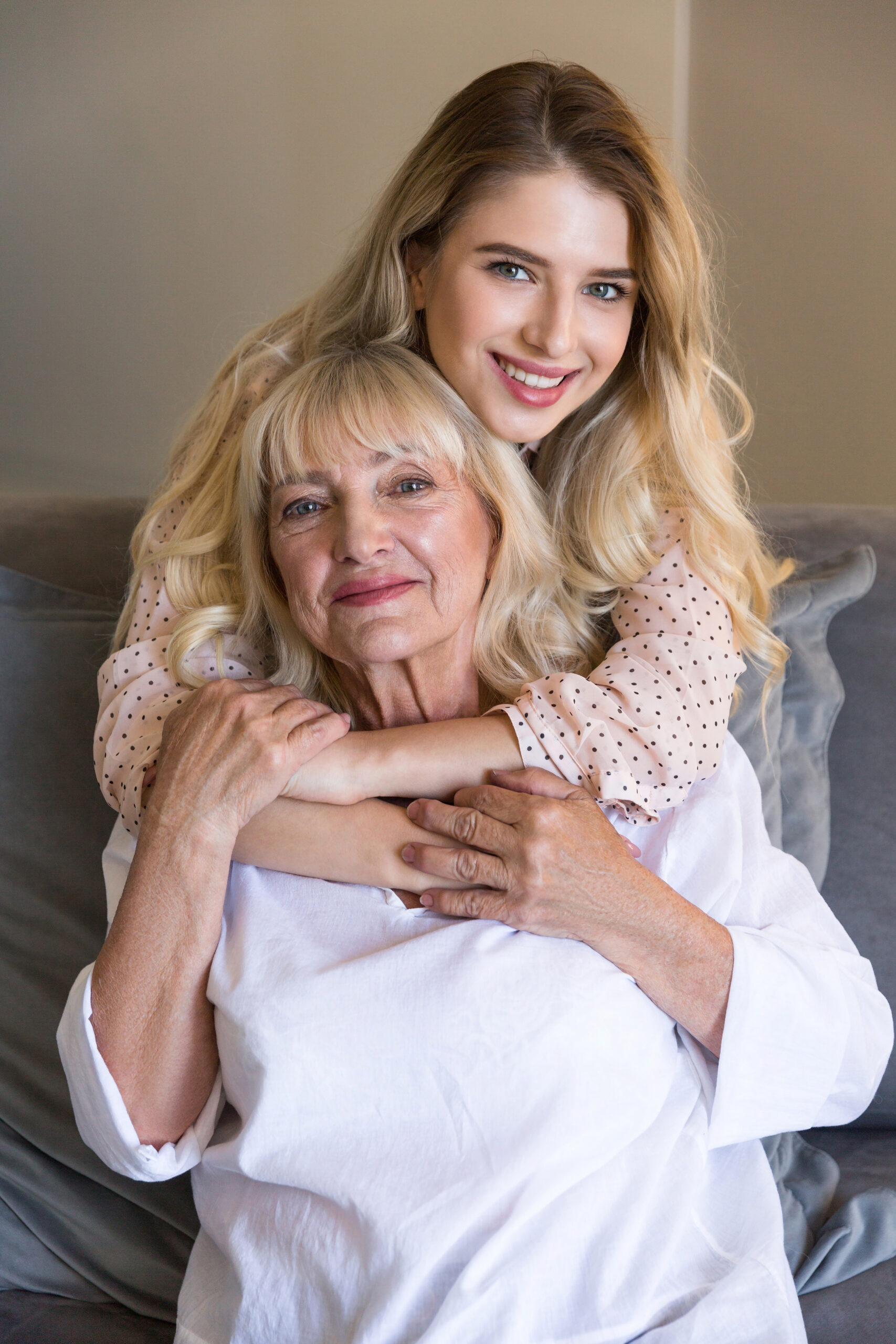Senior woman with granddaughter or daughter hugging on couch at home