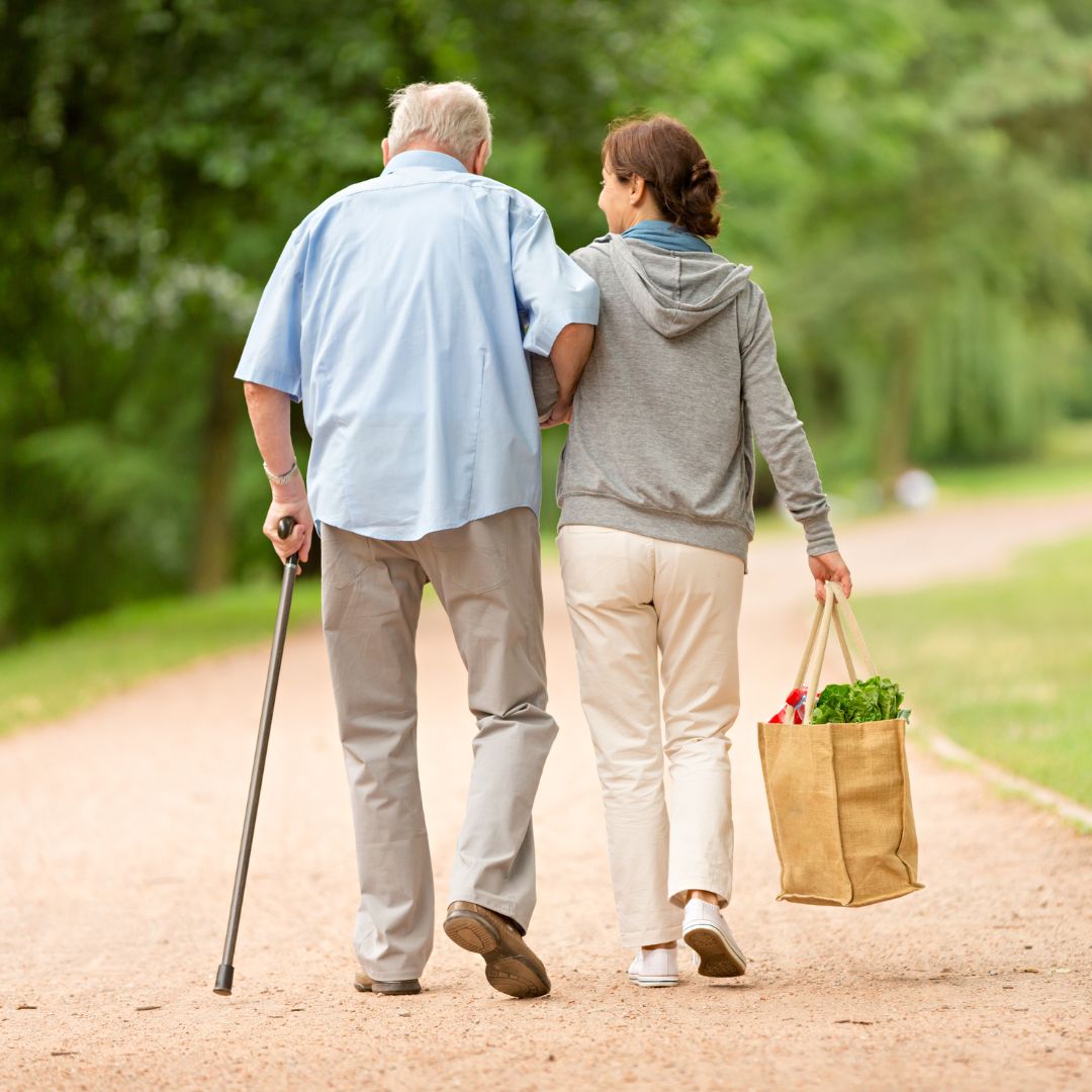 a caregiver carrying a bag and assisting a patient outside on a walk