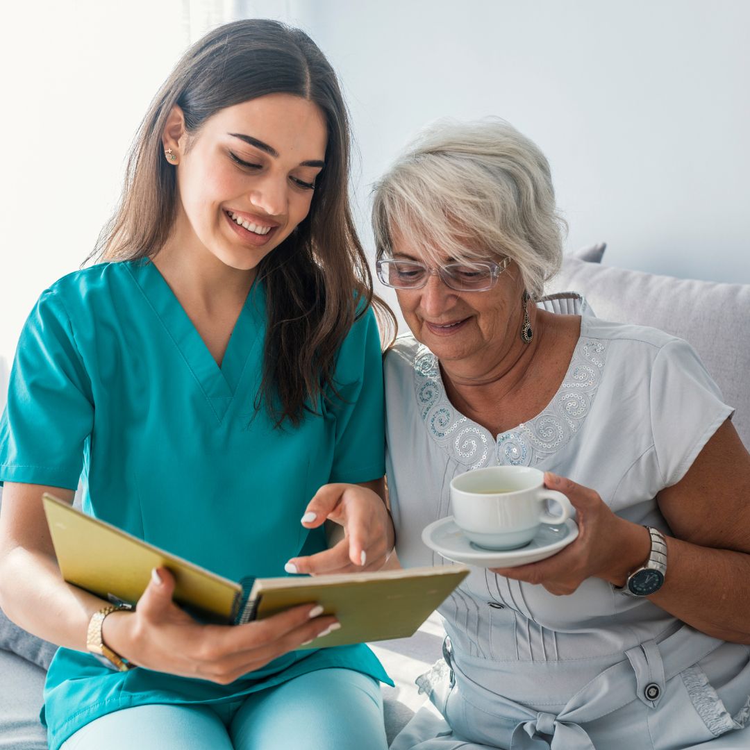 a caregiver and her client looking at a book, drinking a hot beverage
