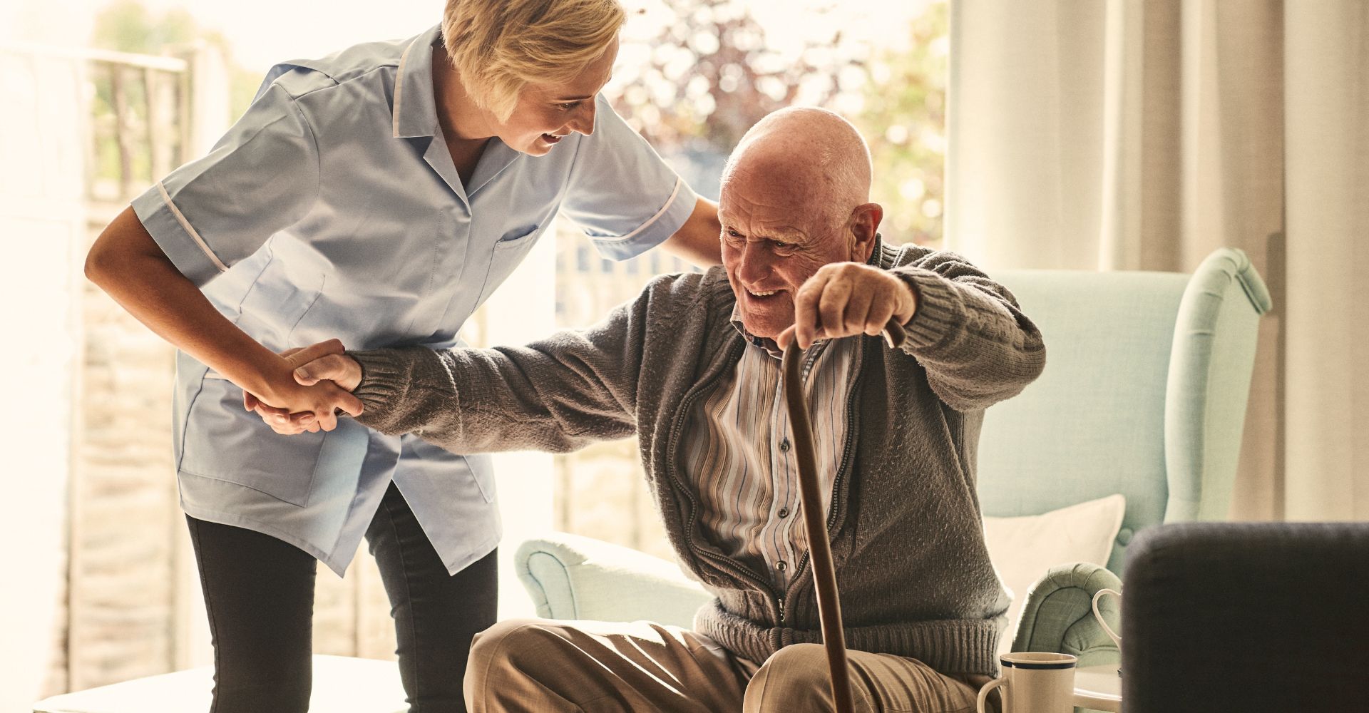A senior being helped up from his seat by an at-home care professional