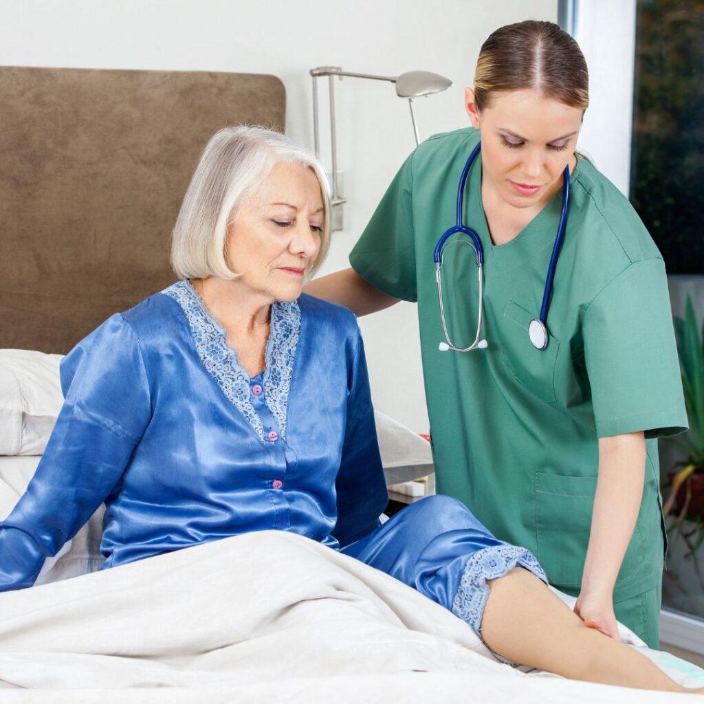 Nurse helping a female patient into bed.