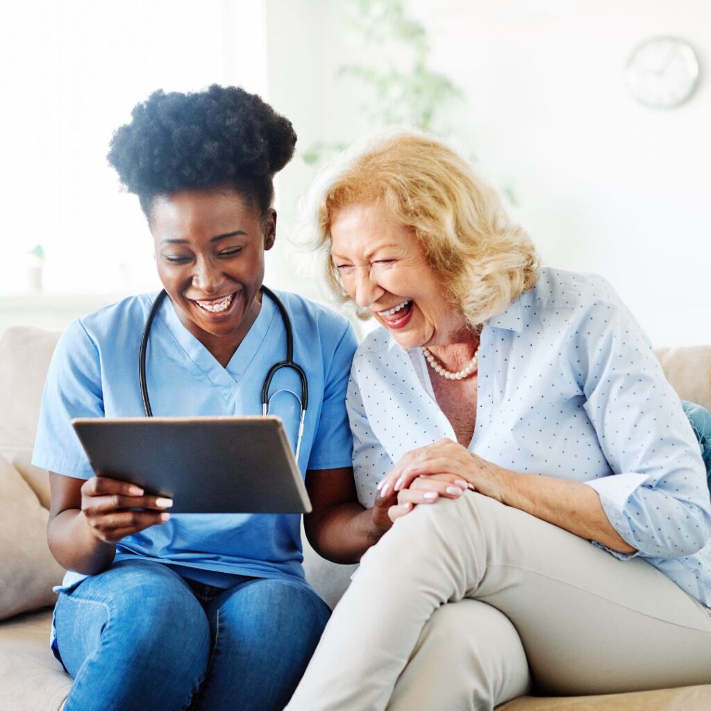 Nurse looking at a tablet while sitting next to a smiling patient.