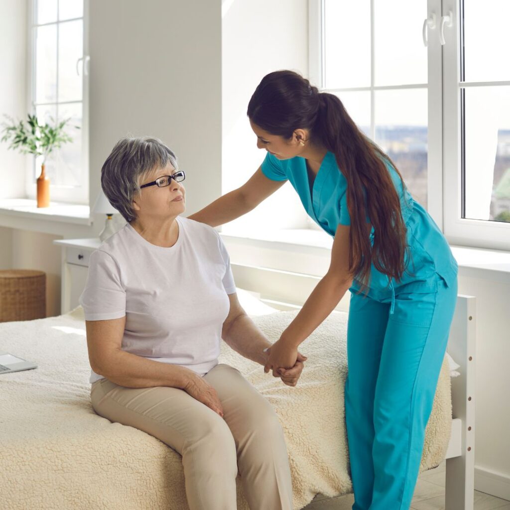 Nurse holding a female patient by the wrist while the patient sits on her bed.